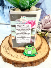 Load image into Gallery viewer, Green frog pin on a wooden coaster with a card and plants in the background